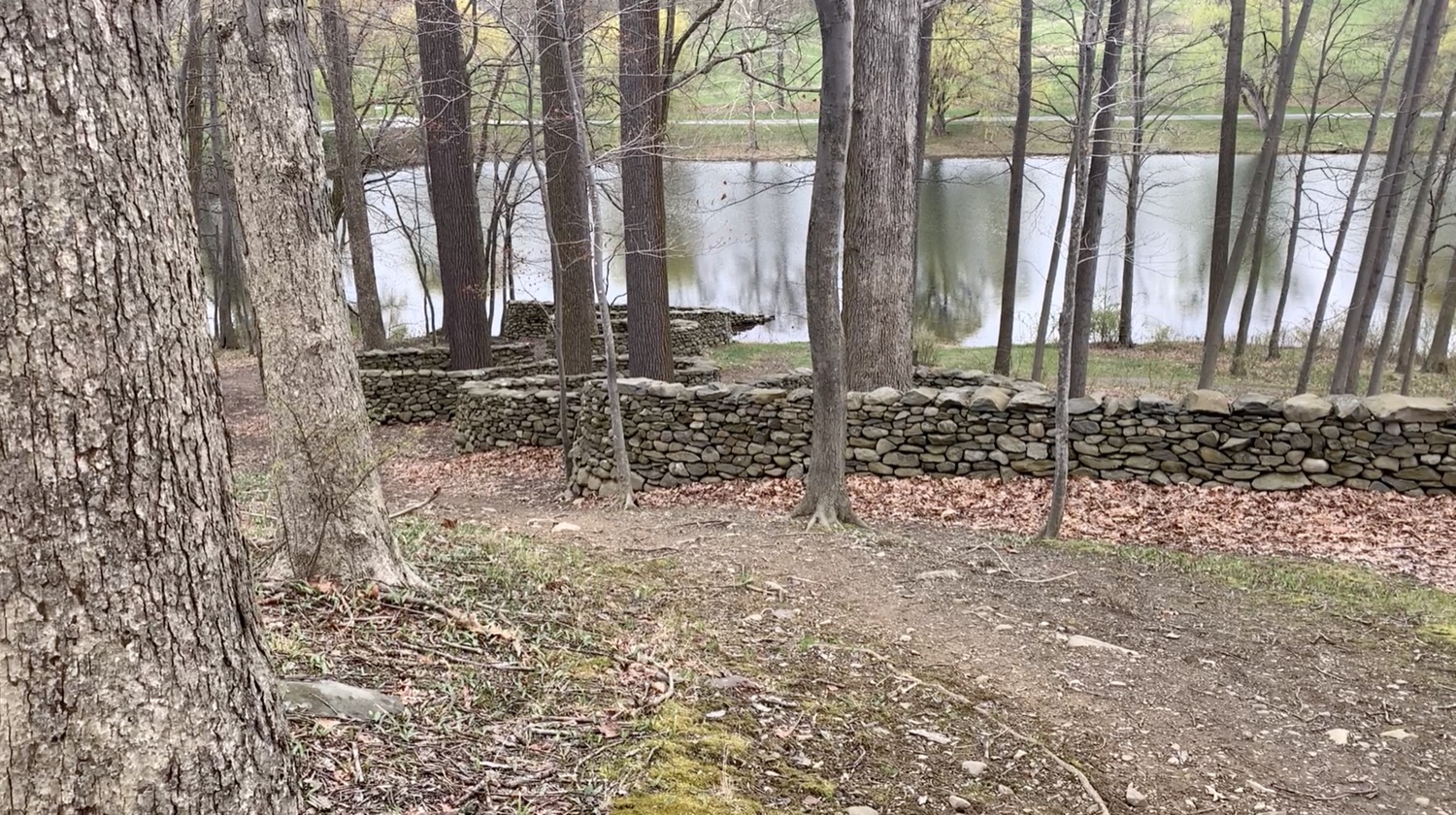 A curving rock wall descending into a pond.